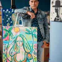 Pedro standing behind a painting of a women on the beach